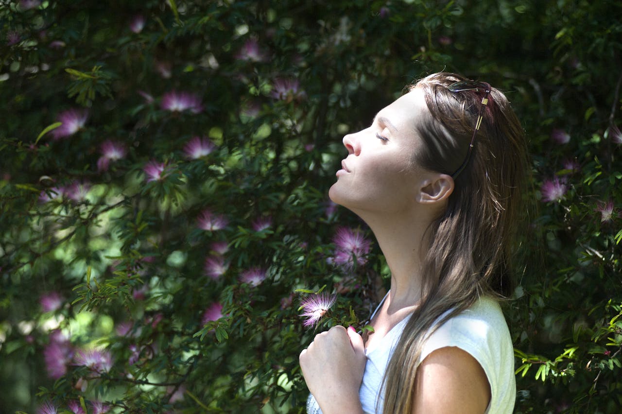 A woman enjoying a serene moment in a sunlit garden, surrounded by vibrant flowers.